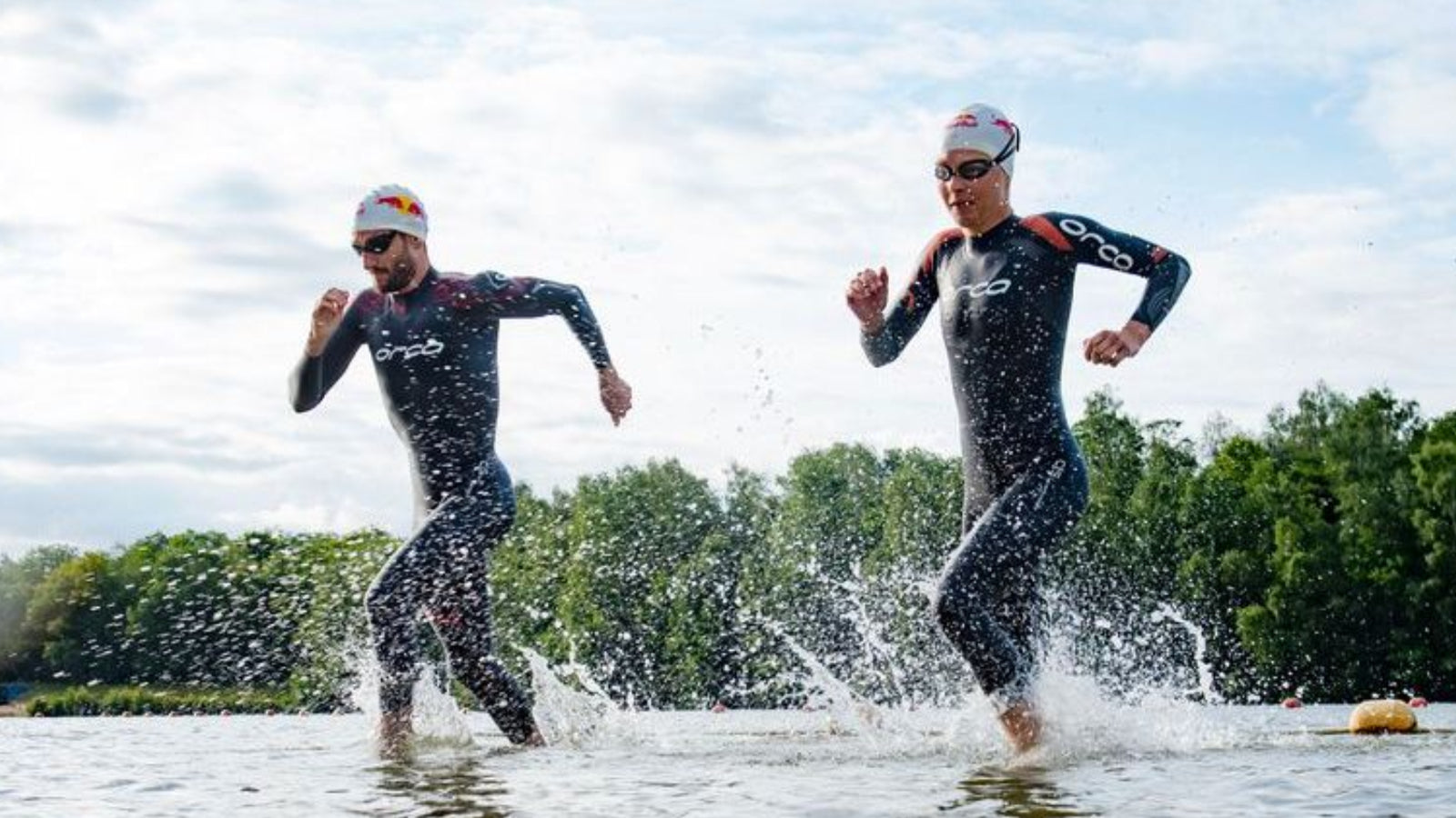 Ein Mann und eine Frau im Neoprenanzug laufen im flachen Wasser eines Sees