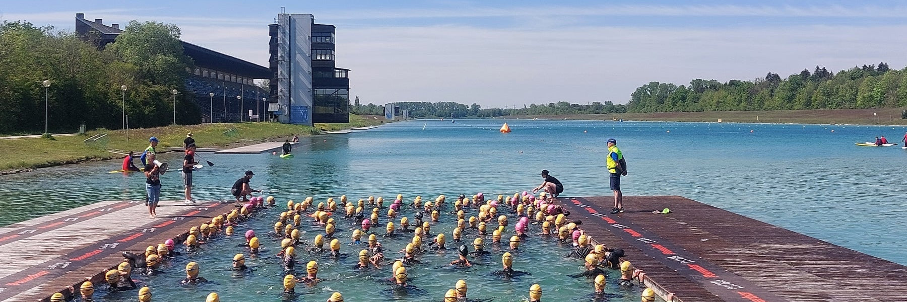 Triathleten mit gelben Badekappen warten im Wasser der Ruderregattastrecke Oberschleissheim auf den Start