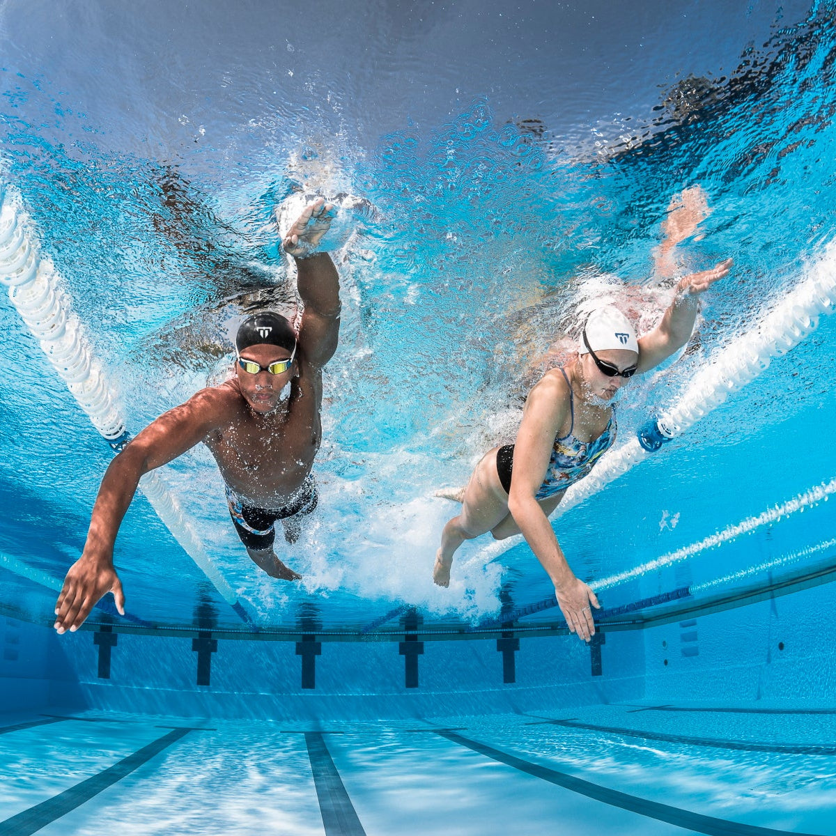 Unterwasseraufnahme von vorn: ein Schwimmer und eine Schwimmerin beim Kraulschwimmen nebeneinander auf einer Schwimmbahn