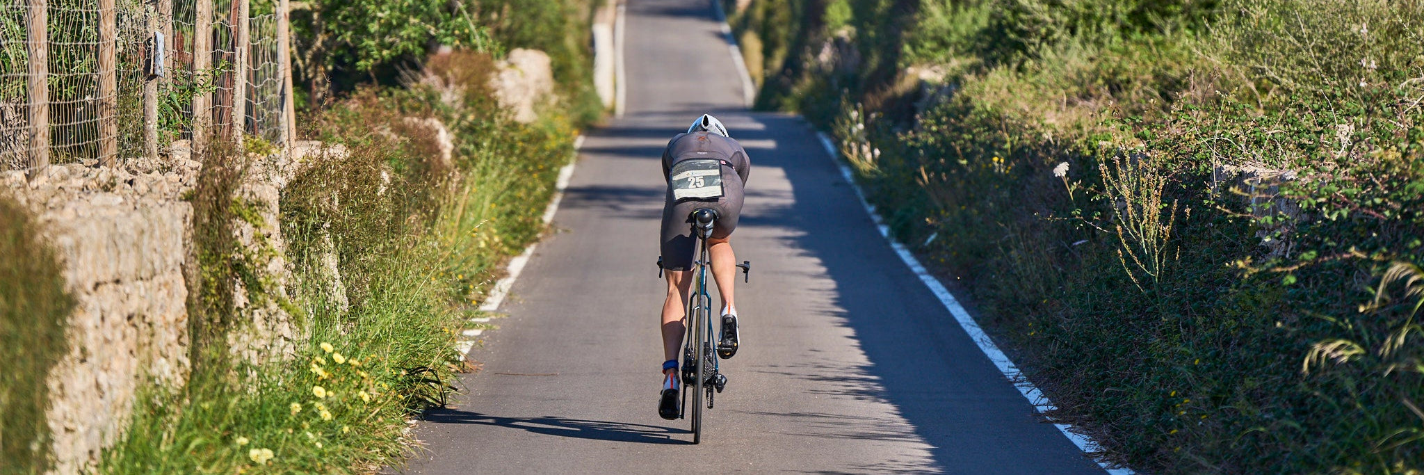 Ein Triathlet auf seinem Fahrrad von hinten fährt auf einer schmalen Straße durch das mallorcinische Hinterland