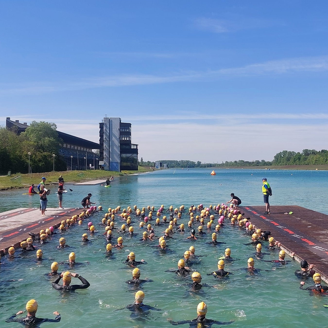 Triathleten mit gelben Badekappen warten im Wasser der Ruderregattastrecke Oberschleissheim  auf den Start